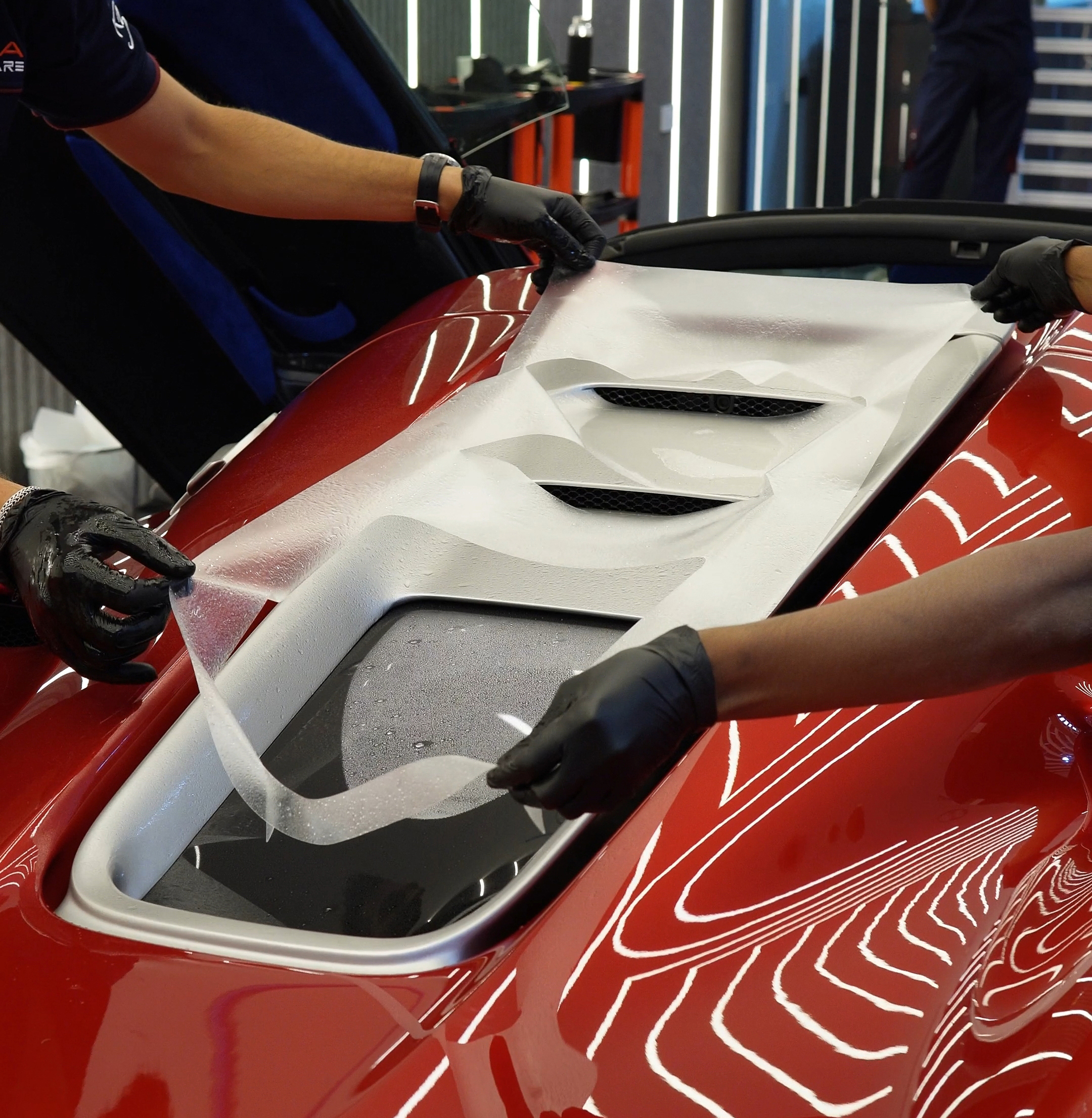 Technicians applying protection film to a red sports car